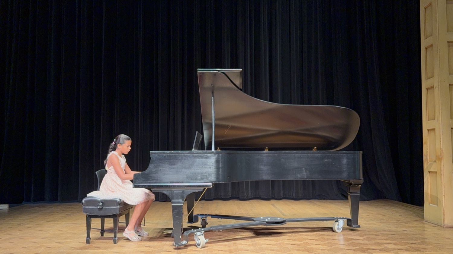 A student in concert dress performing at the grand piano