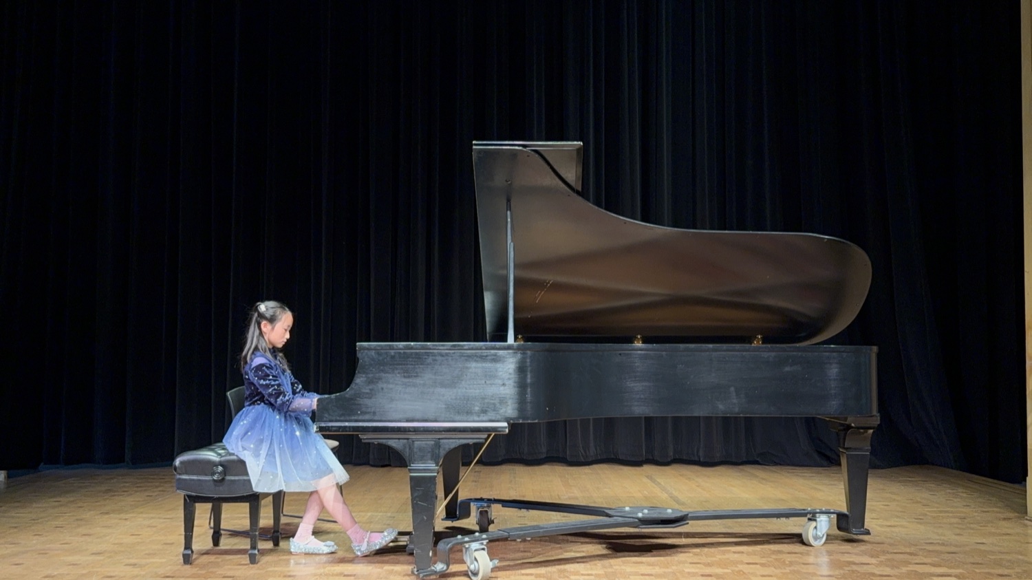 A young pianist in a blue recital dress performing solo